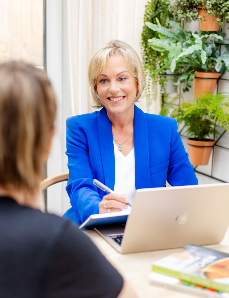Emma-Marshall-consulting-with-client Breast Cancer Nutrition Consultations - Emma Marshall, a white woman with blonde hair, smiles at a client seated at her desk